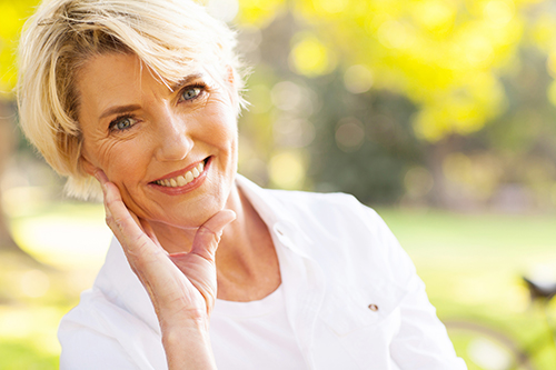 Woman with short hair and white blouse smiling with her head resting in her hand